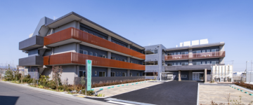 オレンジ色と黒の外壁が特徴の現代的な介護施設の建物外観。複数階建て。