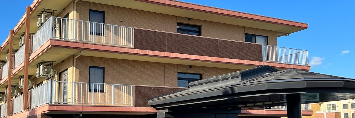 赤いトリムと白いバルコニーを持つ3階建ての介護施設の建物外観